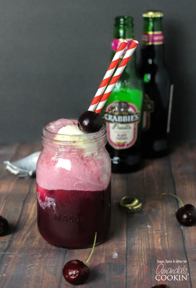 A mason jar filled with a black cherry float cocktail and served with red and white straws.