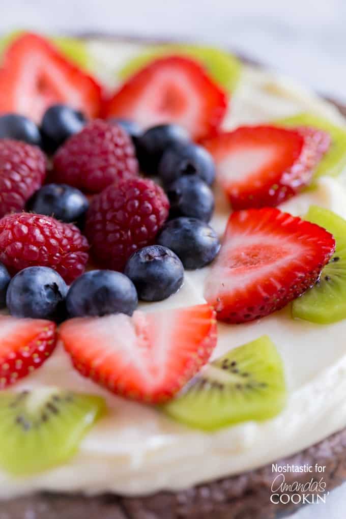 A close up of cut up strawberries, kiwi, blueberries and raspberries on a brownie pizza.