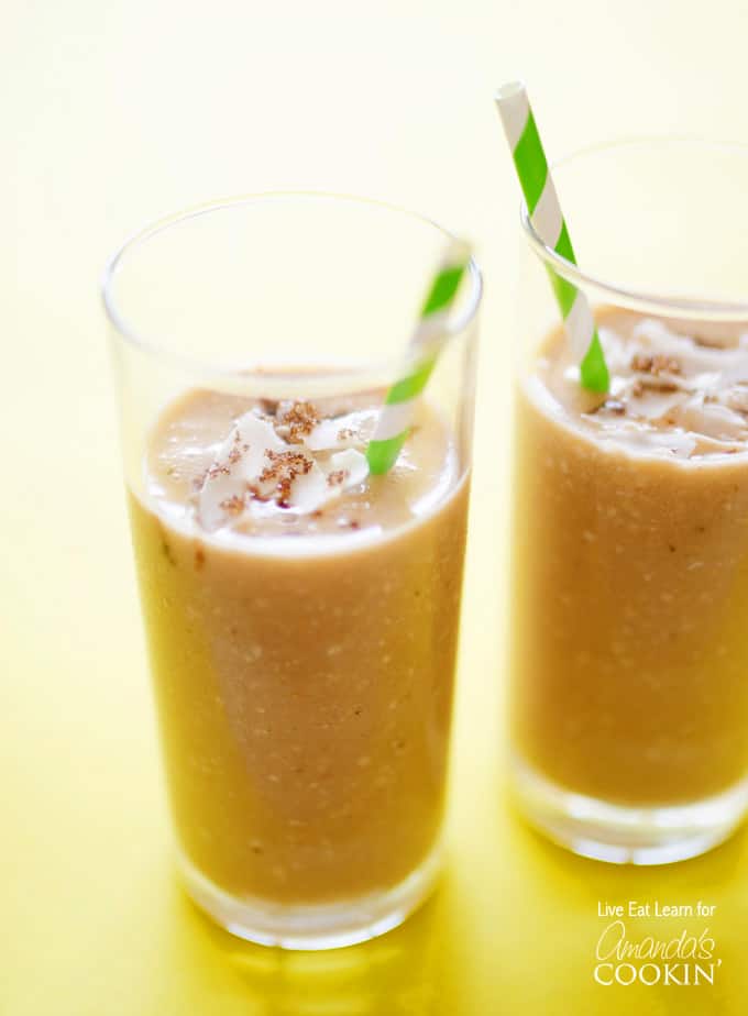 A close up of two tall clear glasses filled with cozy coconut smoothie and served with a green and white striped straw.