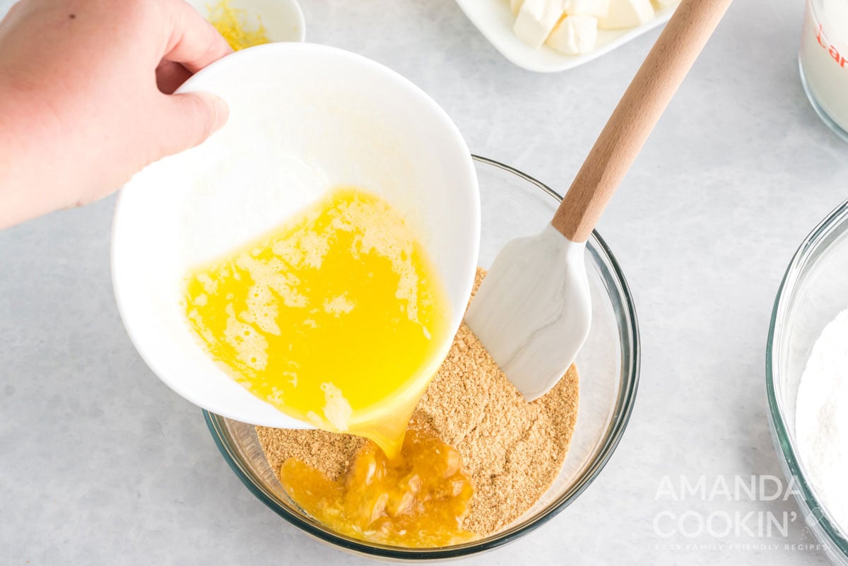 pouring melted butter into a bowl of graham cracker crumbs