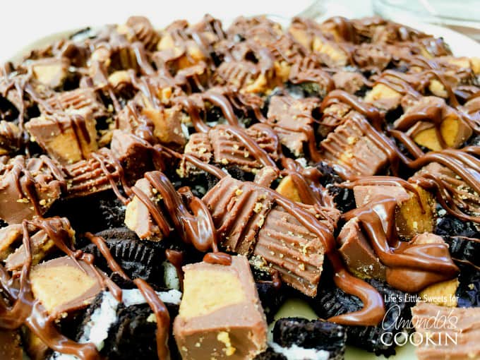 A close up photo of chopped Oreos and peanut butter cups on top of a peanut butter Oreo no bake cheesecake.