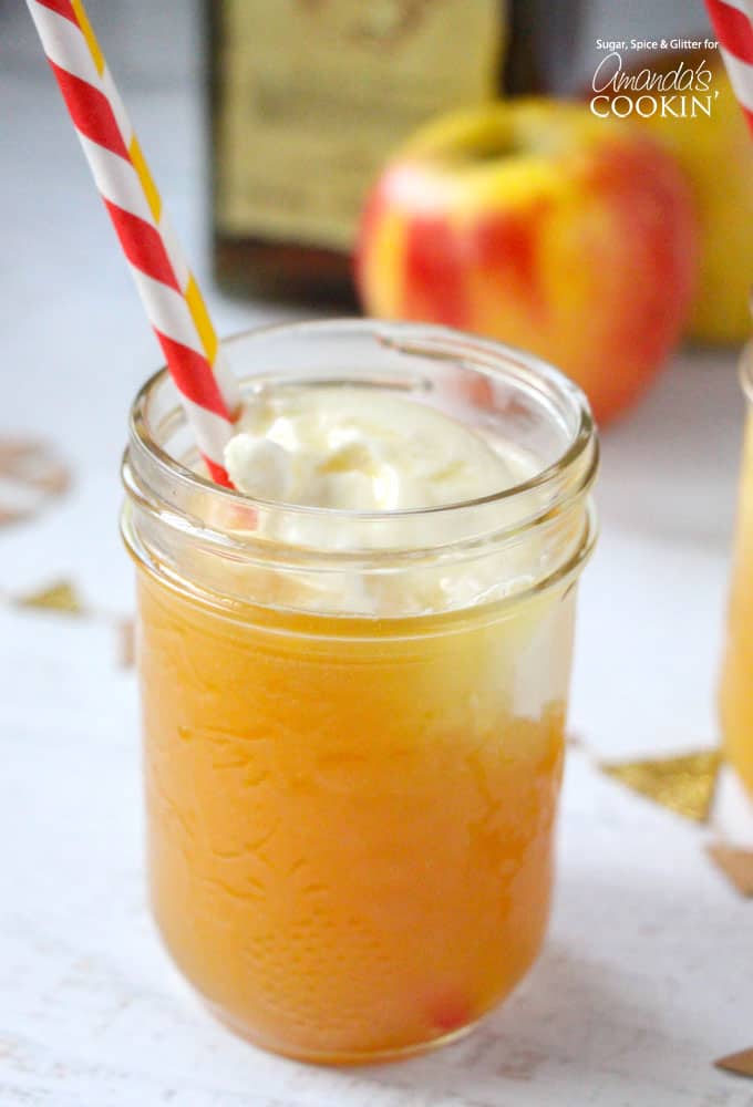 A close up of a mason jar filled with an apple pie cocktail served with a red and white straw.