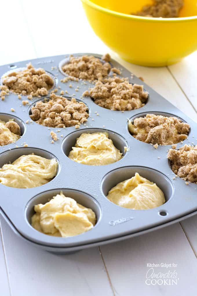 A muffin pan filled with muffin batter and streusel topping on half of them.