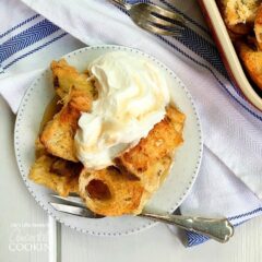 An overhead of french toast casserole on a white plate topped with vanilla whipped cream.
