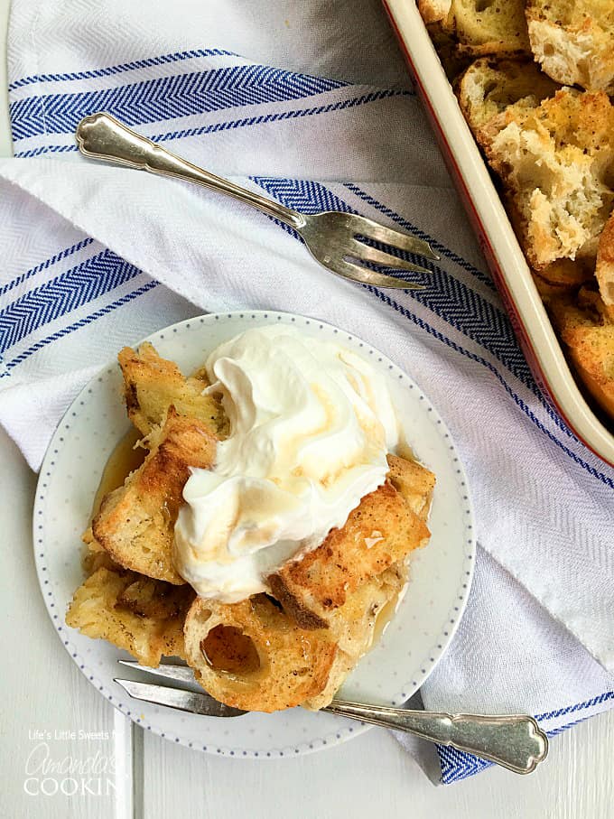 An overhead of french toast casserole on a white plate topped with vanilla whipped cream.