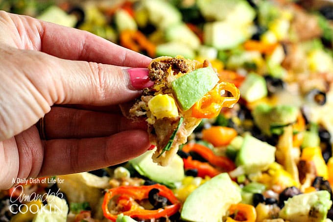 A close up of someone holding a tortilla chip with taco meat, avocado, and corn.