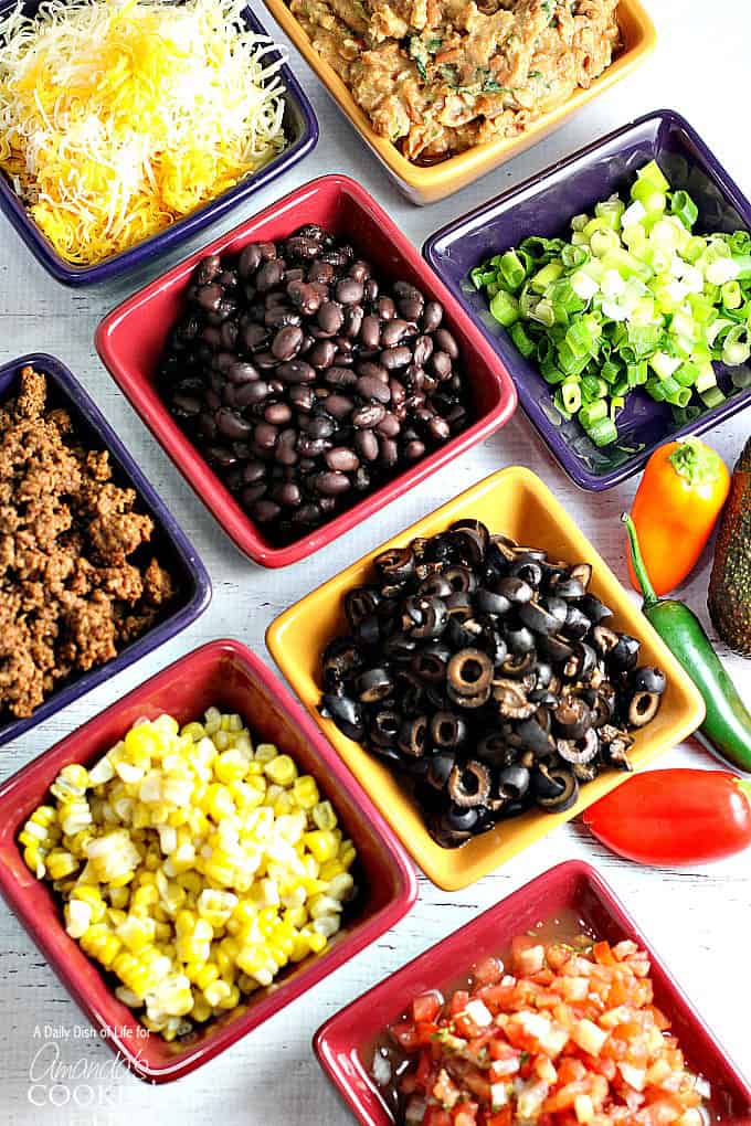 A variety of square bowls filled with taco meat, corn, black beans, black olives, green onions and cheese.