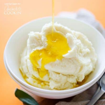 A white bowl filled with cauliflower mashed potatoes and melted butter on top.