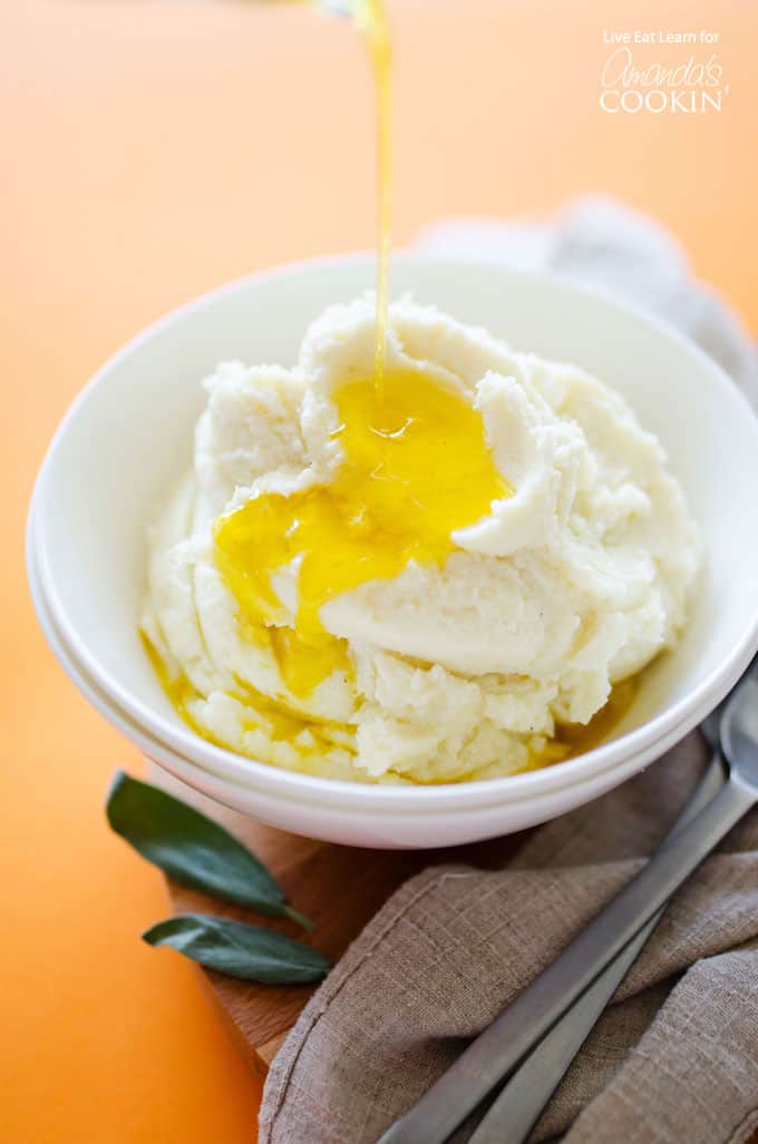 A white bowl filled with mashed cauliflower and melted butter on top.