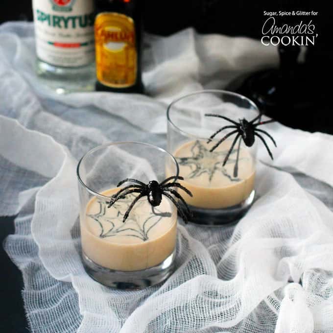 Two clear glasses filled with a spiderweb in cream martini and a fake spider on the glass.