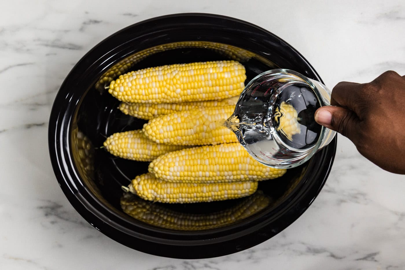 pouring water into crockpot that has cob in it