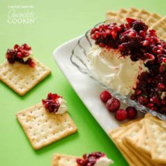 Cranberry salsa spooned over cream cheese in a glass dish with cracker squares surrounding.