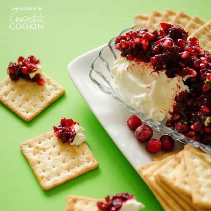 Cranberry salsa spooned over cream cheese in a glass dish with cracker squares surrounding. 