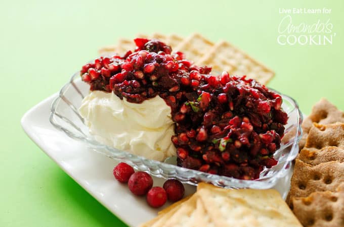 Cranberry salsa spooned over cream cheese in a glass dish with cracker squares surrounding. 