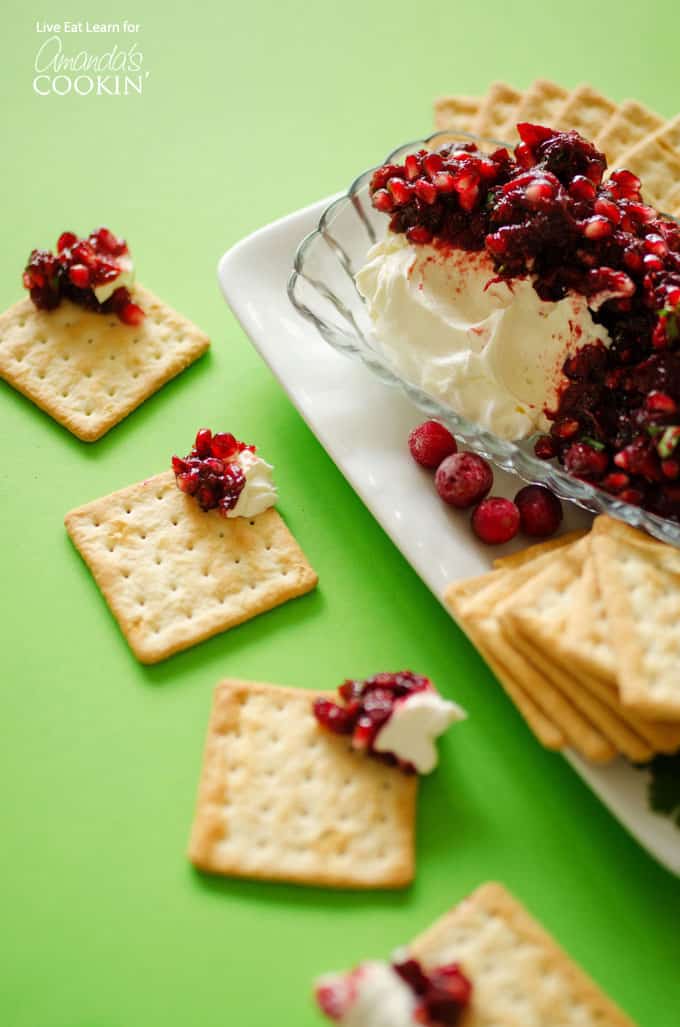 Cranberry salsa spooned over cream cheese in a glass dish with cracker squares surrounding. 