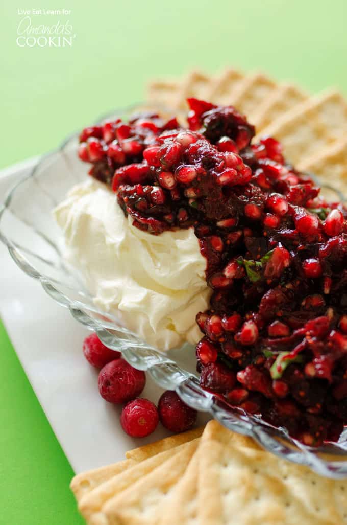 A close up of cranberry salsa spooned over cream cheese in a glass dish.