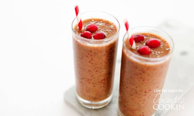 A close up of two cranberry smoothies with cranberries on top and served with a straw.