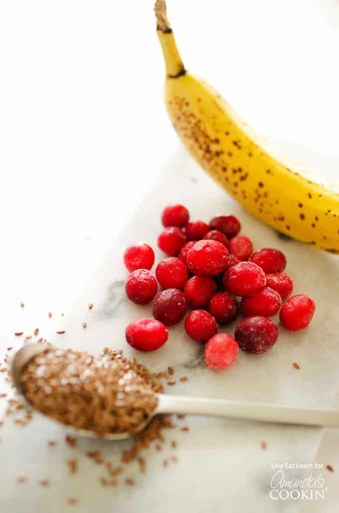 A photo of a banana, cranberries and spoonful of flax seeds.
