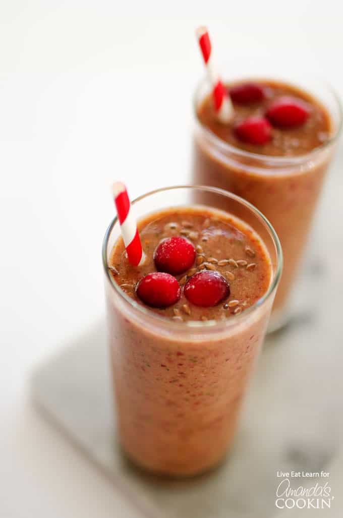 A close up overhead of two cranberry smoothies with cranberries on top and served with a straw.