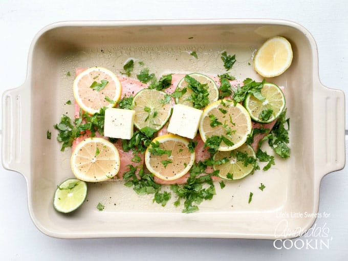 An overhead photo of salmon resting in a baking dish covered in lemon and lime wheels topped with fresh cilantro.