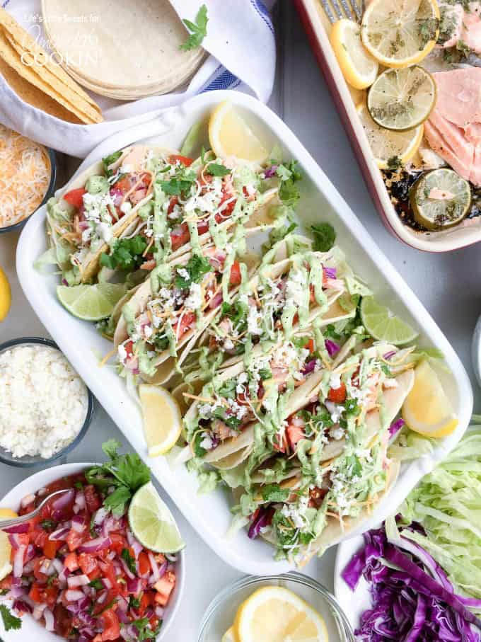 An overhead photo of salmon tacos resting in a casserole dish with lemon and lime wedges on the side.