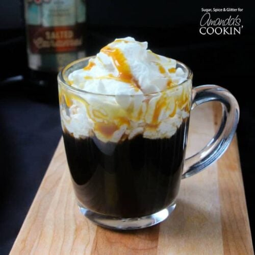 A salted caramel coffee cocktail in a clear mug with whipped cream and drizzled caramel on top.
