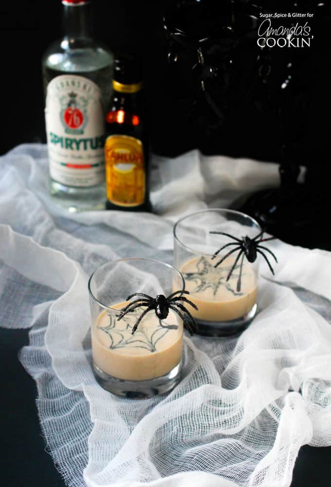 Two clear glasses filled with a spiderweb in cream martini and a fake spider on the glass.