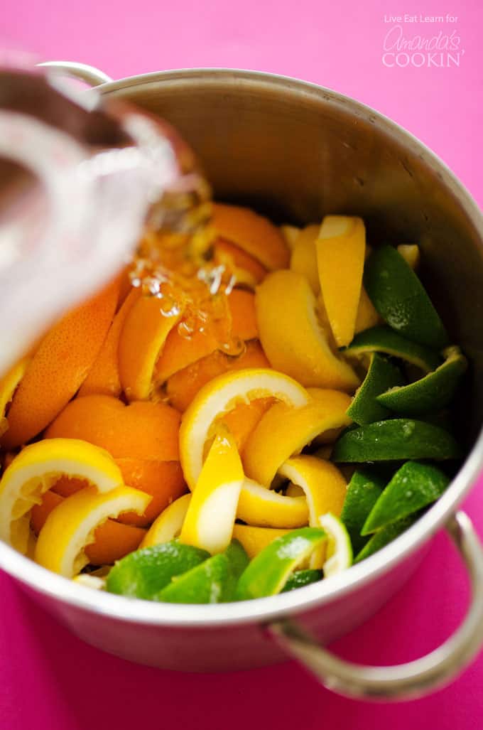 A large pot filled with orange, lemon, lime and grapefruit peels with water being poured in.