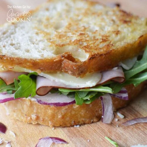 A close up of a toasted cheddar, ham and arugula sandwich.