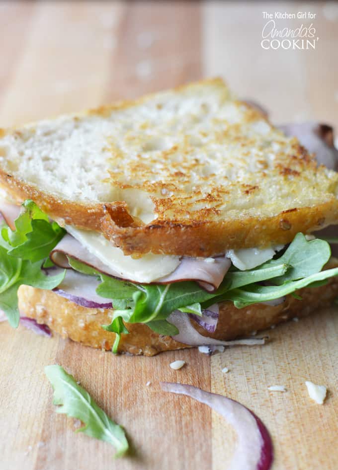 A close up of a toasted cheddar, ham and arugula sandwich.