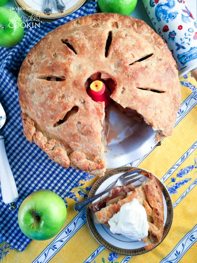 A whole homemade apple pie with a missing slice that is sitting on a plate to the side.