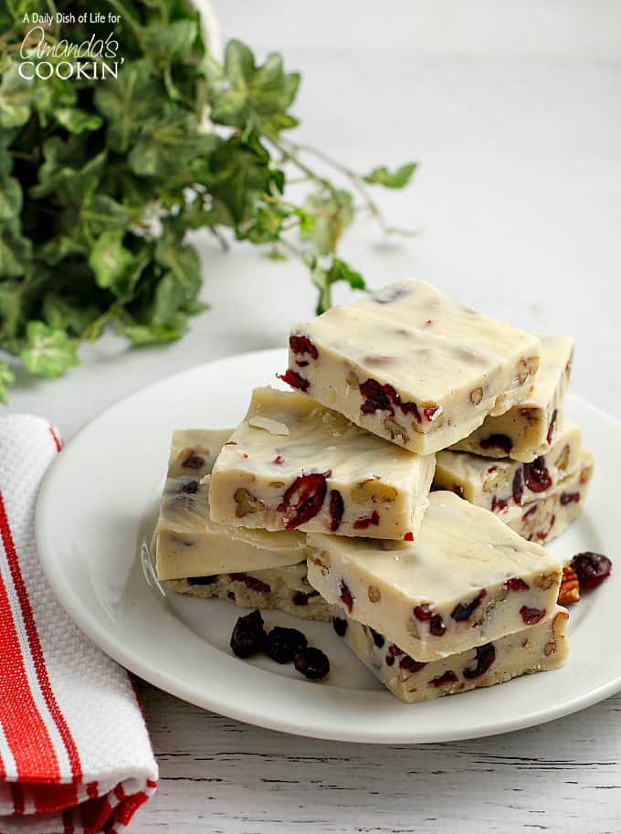 Squares of white chocolate cranberry fudge stacked on a white plate.