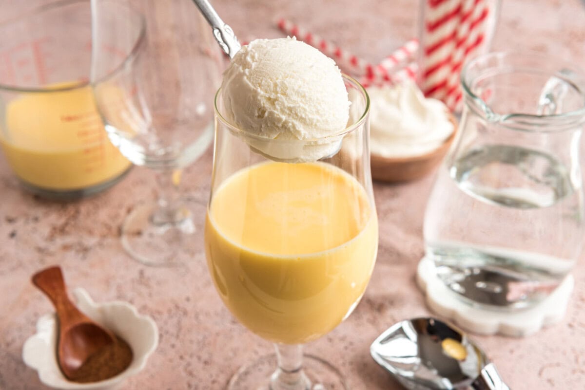 adding a scoop of vanilla ice cream to glass with eggnog