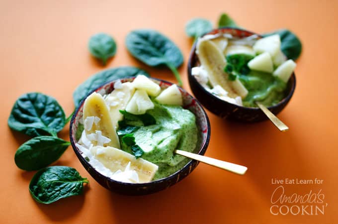 A close up of two pineapple spinach smoothie bowls with spinach resting in the background. 