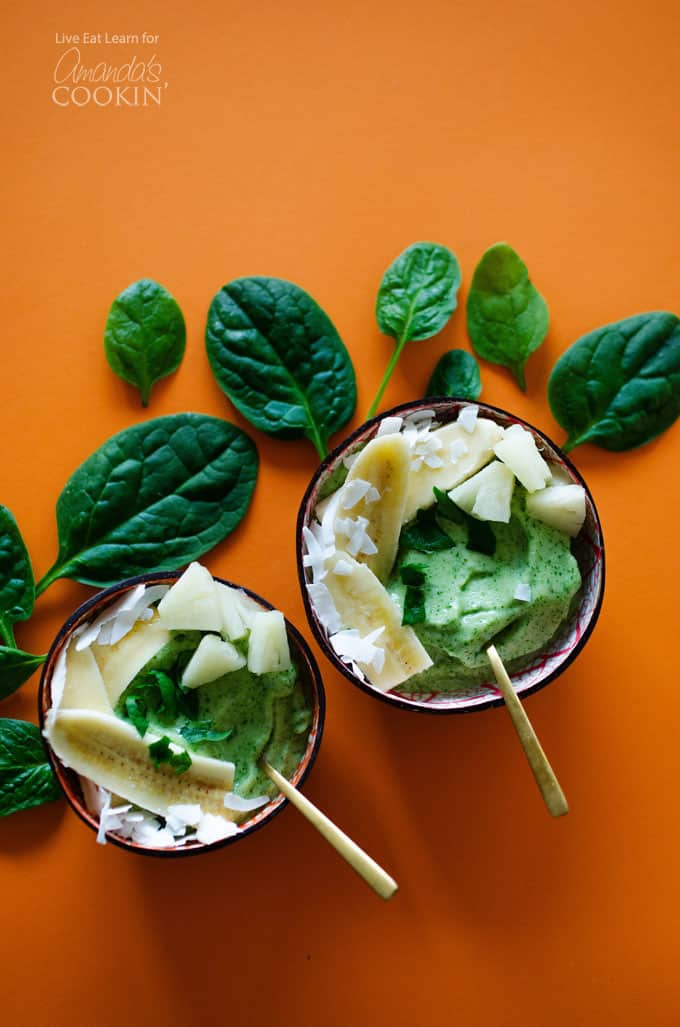 An overhead of two pineapple spinach smoothie bowls with spinach leaves on the table.