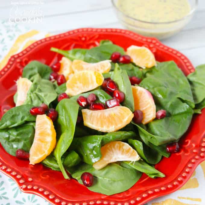 A pomegranate clementine spinach salad on a red plate.