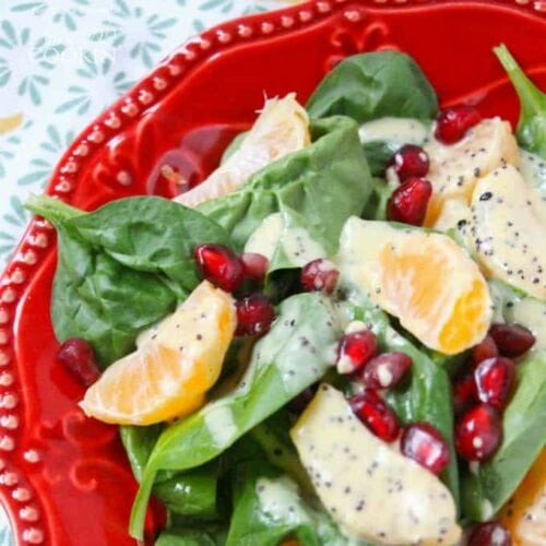 A close up of a pomegranate clementine spinach salad on a red plate.