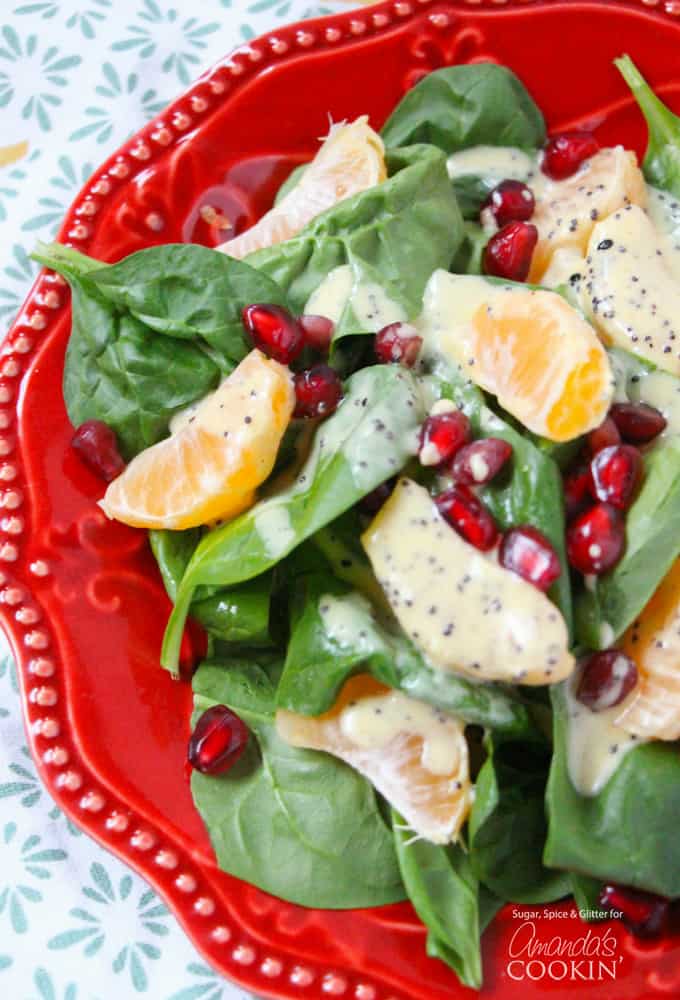 A close up of a pomegranate clementine spinach salad on a red plate.