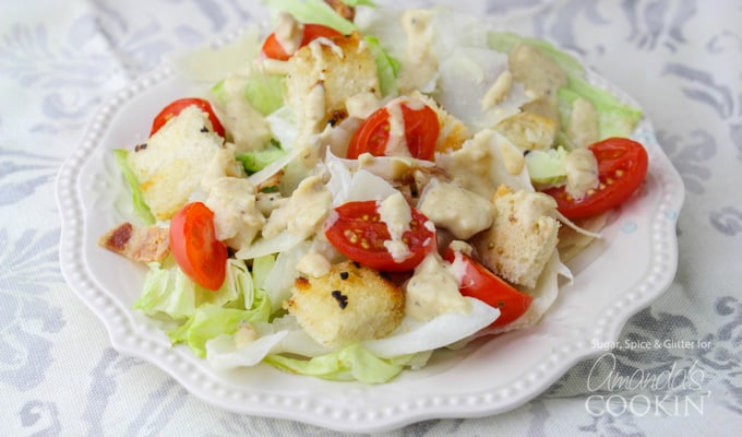 A close up of a tomato Caesar salad on a white plate.