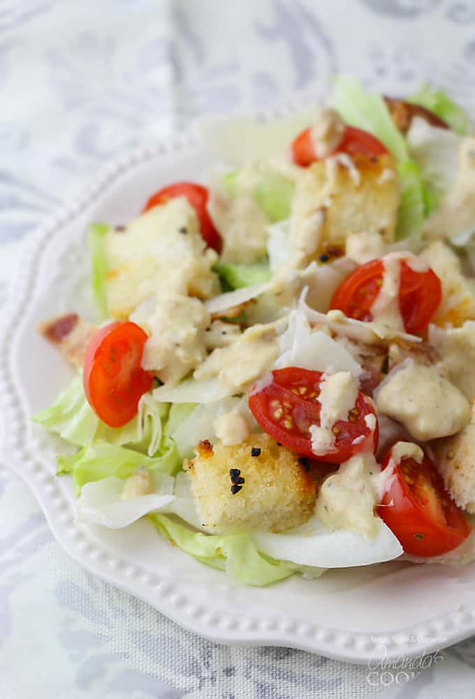 A close up of a tomato Caesar salad on a white plate.