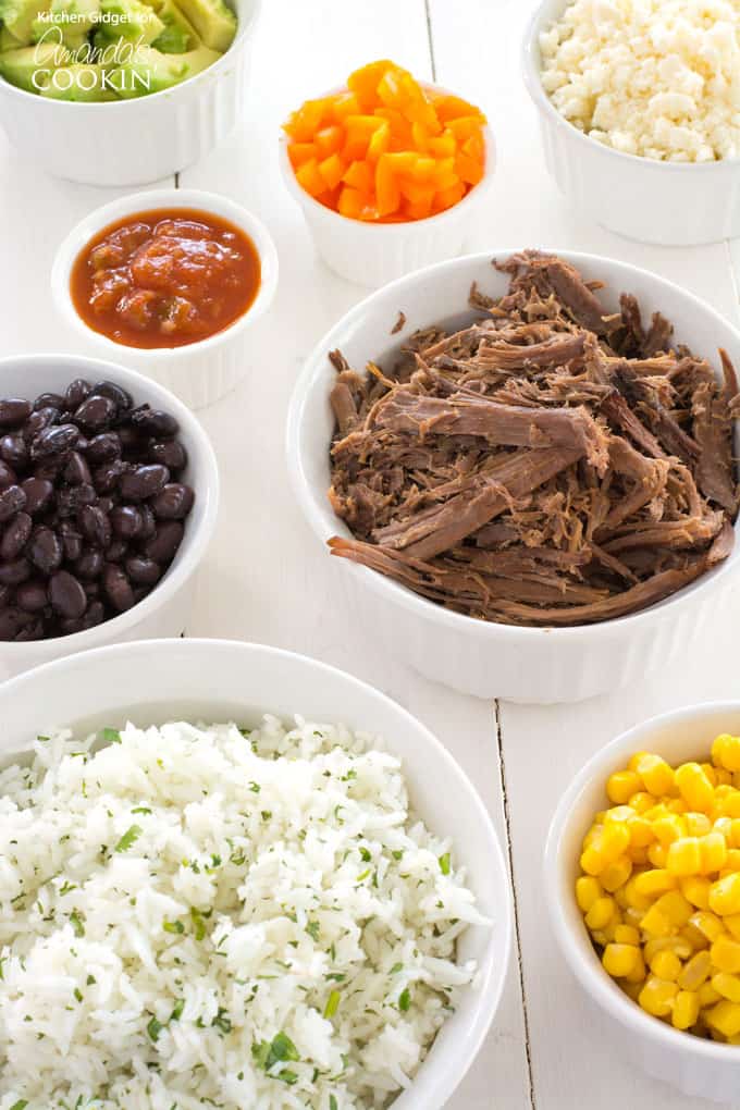 Multiple little white bowls filled with cooked beef, white rice, black beans and corn.