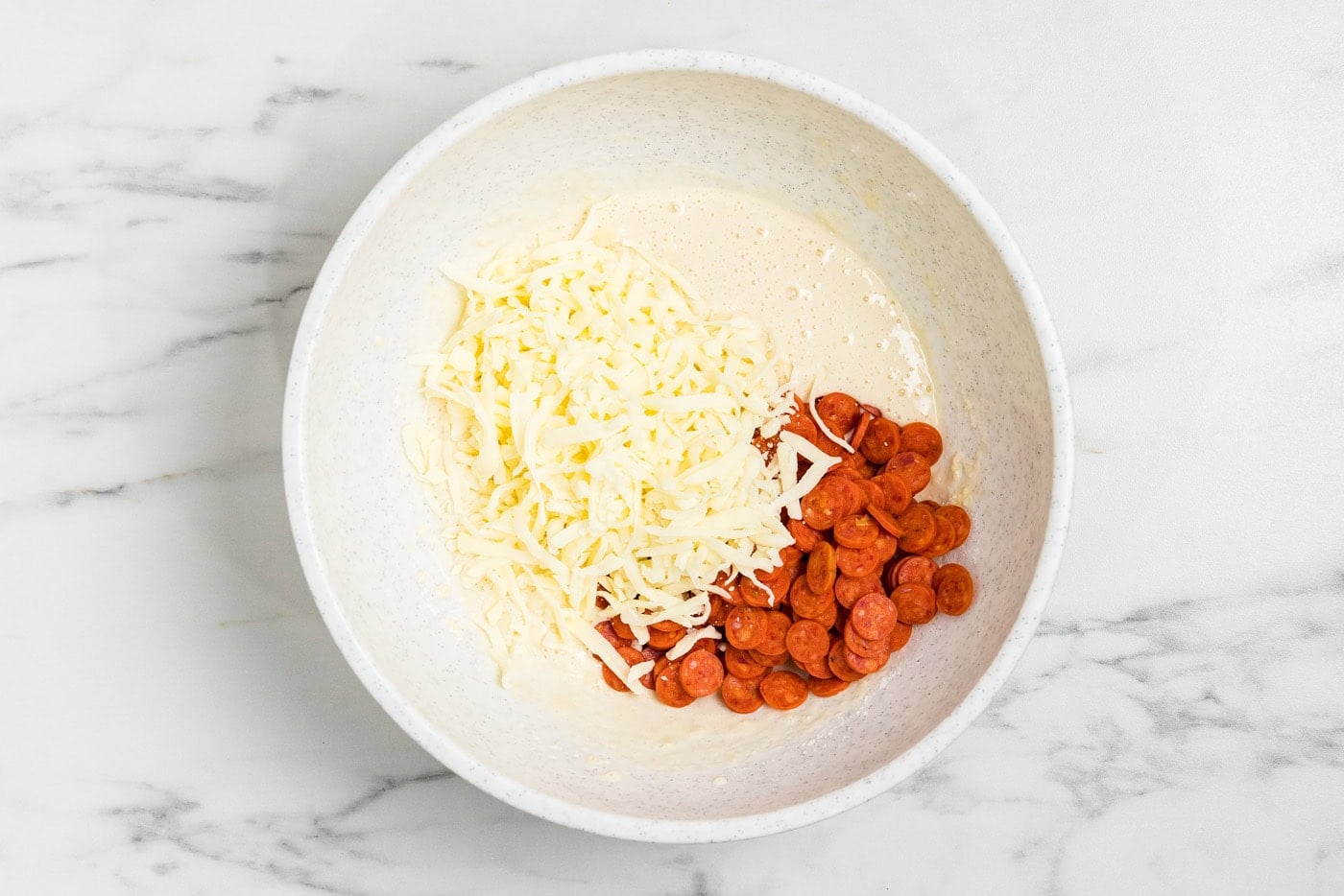 shredded cheese and mini pepperonis in bowl with batter