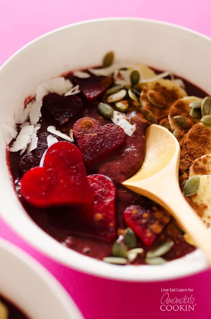 A close up of a white bowl filled with a red velvet smoothie and a wooden spoon.