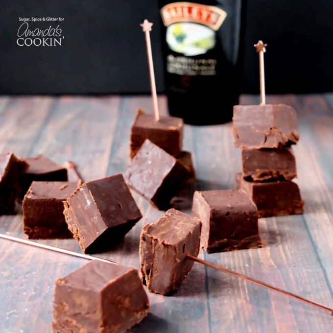 Squares of Bailey\'s fudge resting on a wooden cutting board with a bottle of Bailey\'s in the background.
