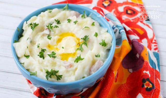 A blue bowl filled with Colcannon mashed potatoes topped with chopped parsley and melted butter.