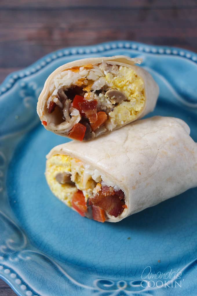 A close up picture of a breakfast burrito cut in half resting on a blue plate.