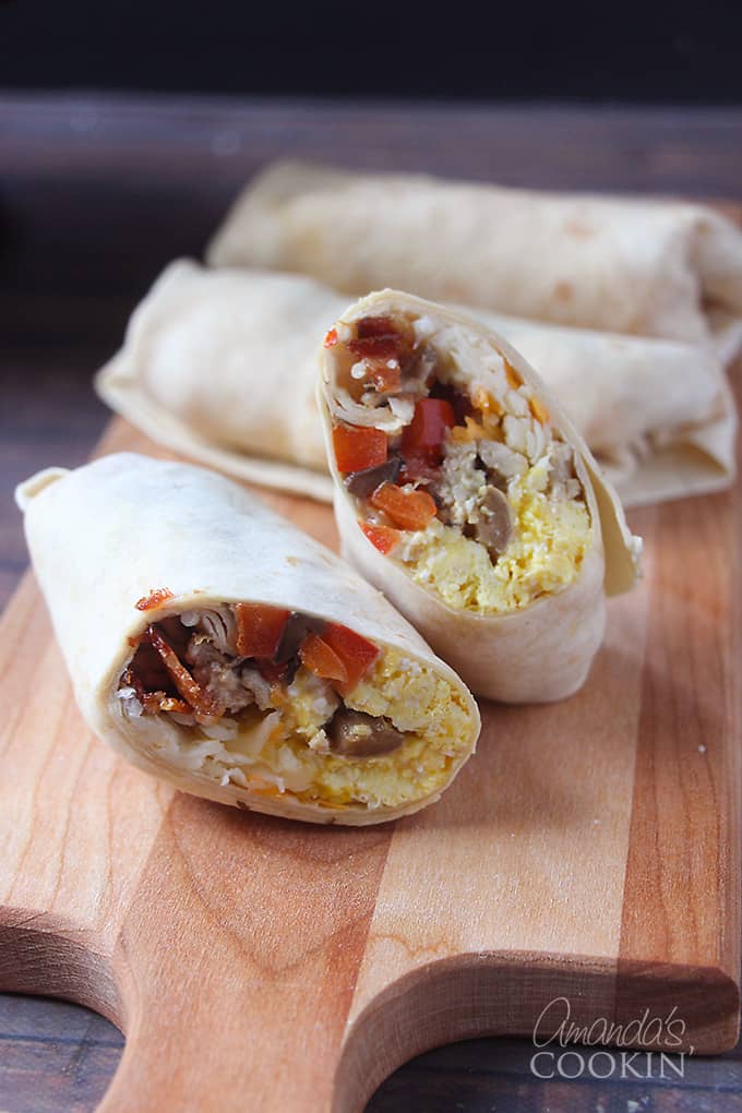 A breakfast burrito cut in half with one side stacked on the other with whole burritos in the background all resting on a wooden cutting board.