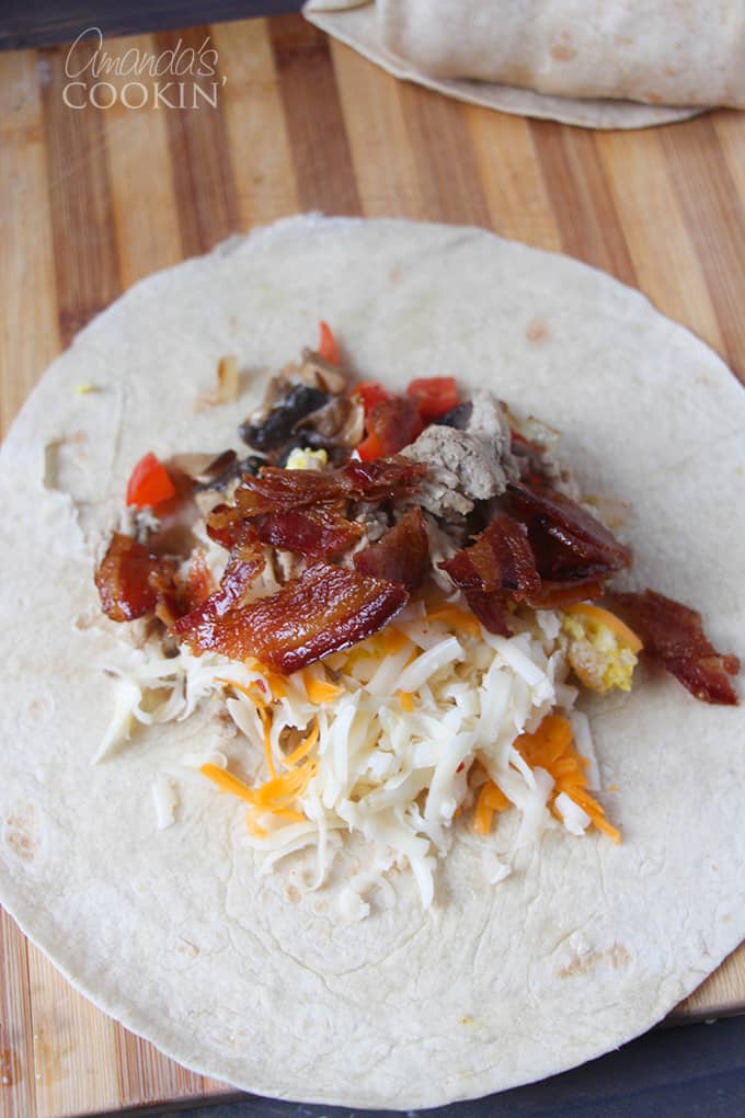 An overhead picture of an open tortilla with cheese, bacon and scrambled eggs laying on a wooden cutting board.