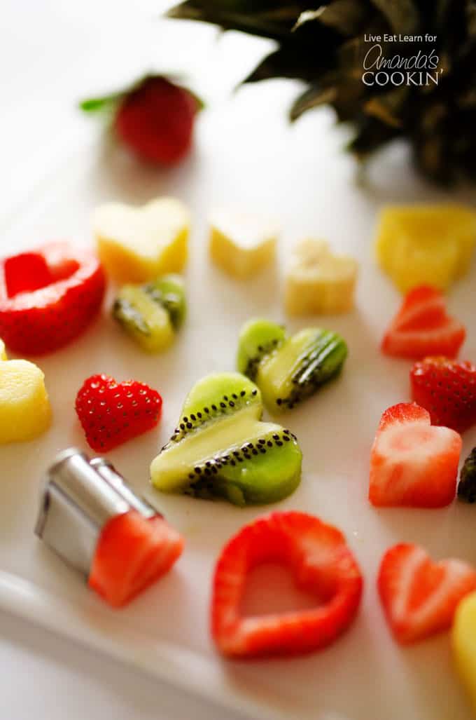 Fresh fruit cut into hearts resting on a white cutting board.