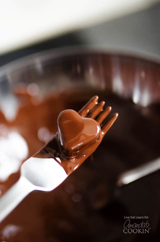 A fork holding a fruit heart that was just dipped in chocolate.
